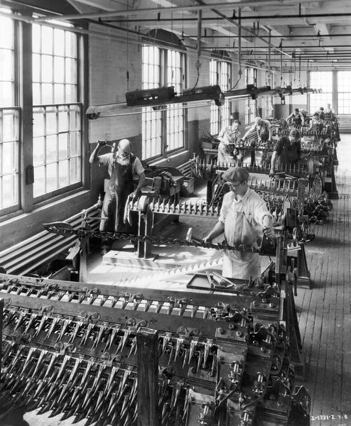 Elevated view of workers building sickle bars for mowers at International Harvester's McCormick Works. The McCormick Works was built by Cyrus McCormick in 1873 and became part of International Harvester in 1902. The factory was located at Blue Island and Western Avenues in the Chicago subdivision called "Canalport." It was closed in 1961.