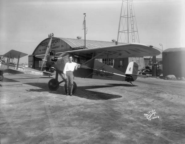 W.L. Pinney, general manager of the Madison Airport (aka North Street Airport) and the Midwest Air Transport Company, stands by the company's two seat "Super Cardinal" C2-110. Facilities of the airport in view include the hangar, windsock, and tower of the 24-inch rotating beacon light.
