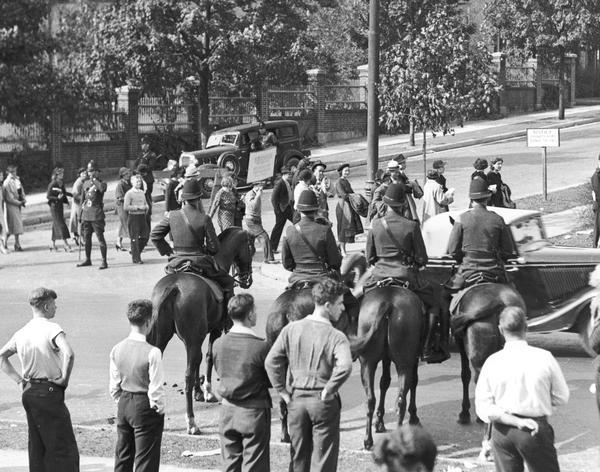 Four police officers on horses watch picketers cross a street.