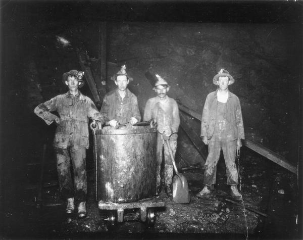 Zinc miners posing with an ore bucket down in a mine.