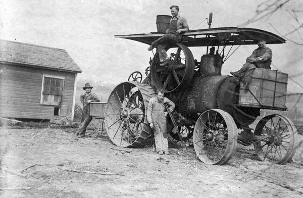 Steam tractor; two men are seated on the tractor and two men are standing leaning against it.  One man has crutches under one arm.
