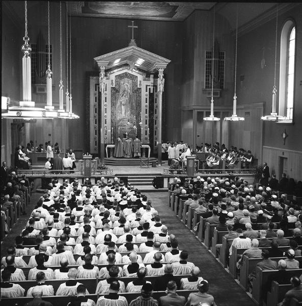 Re-dedication of St. Raphael's Cathedral. Elevated view of people sitting in pews for a service. Newspaper caption reads: "Resplendent St. Raphael Cathedral Shown in It's [sic] New Raiment at Thursday's Solemn Pontificial [sic] Mass."