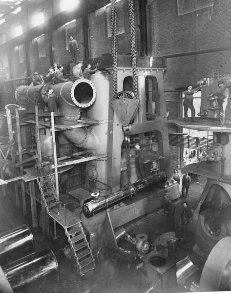 Men standing on and around an Allis steam pump in a factory.
