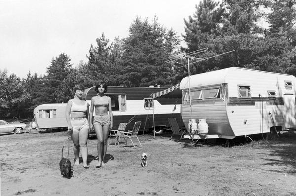 Two women in bikinis are walking their dogs by a row of campers at Terry Andrae State Park.