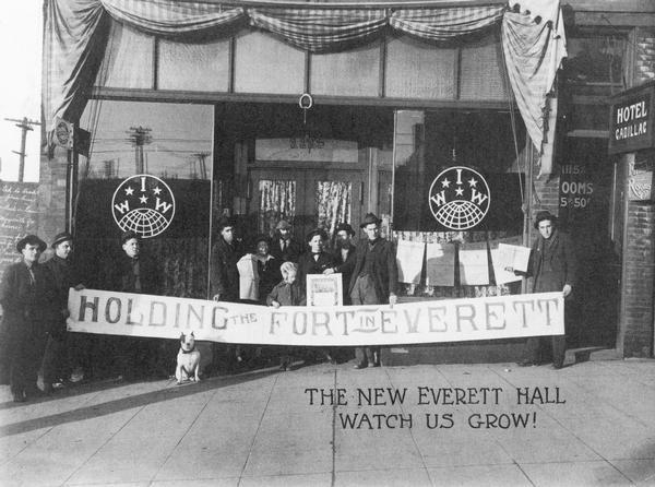 Workers in front of the new I.W.W. Hall in Everett holding a banner which reads "Holding The Fort In Everett". The first hall was destroyed by vigilantes.