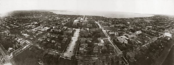 Kite aerial panoramic photograph of the central business district. In the distance is Lake Mendota. The fire damaged Wisconsin State Capitol is in the center of the image, with the west wing of the present capitol nearing completion.