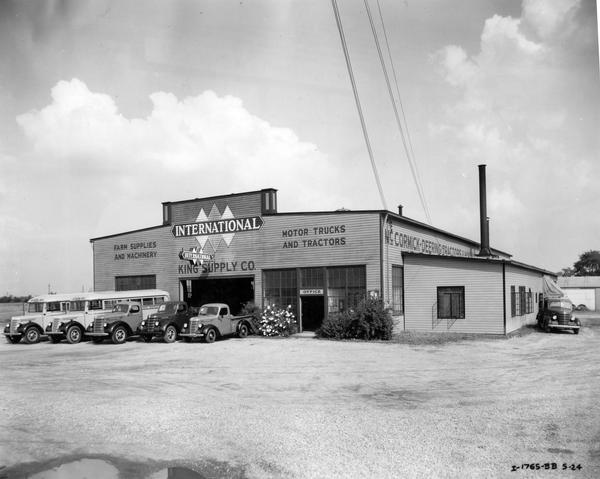 International school buses and trucks lined up outside the dealership building of King Supply Co. The dealership also sold farm equipment and supplies.