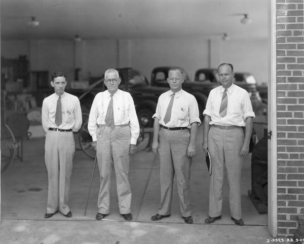 Employees lined up in the service entrance of Whiddon Implement and Truck Company, an International Harvester dealership. Left to right are Alvin Mount, truck salesman, A.D. Whiddon, Beatty Whiddon, and O.I. Cunningham, sales promotion man of Birmingham. Farm equipment and trucks are in background. Image taken for the article: "One of the Most Modern Stores in the South", International Harvester Dealer, March 1939.