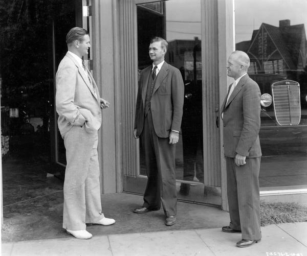 Three men standing outside the International motor truck dealership of the Drew Carriage Company. Left to right are E.W. Drew, F.A.C. Drew and E.B. Hershberger, advertising man for the Los Angeles branch.