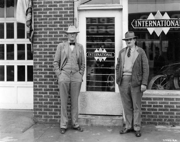 Two men standing outside the front entrance to the Powell-Cavanaugh Truck and Tractor Company. The dealership sold trucks and farm equipment.