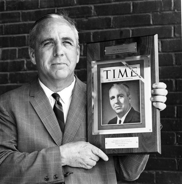 John M. Alexander holding plaque recognizing him as the Time/North American Dealer Association (NADA) truck dealer of the year.