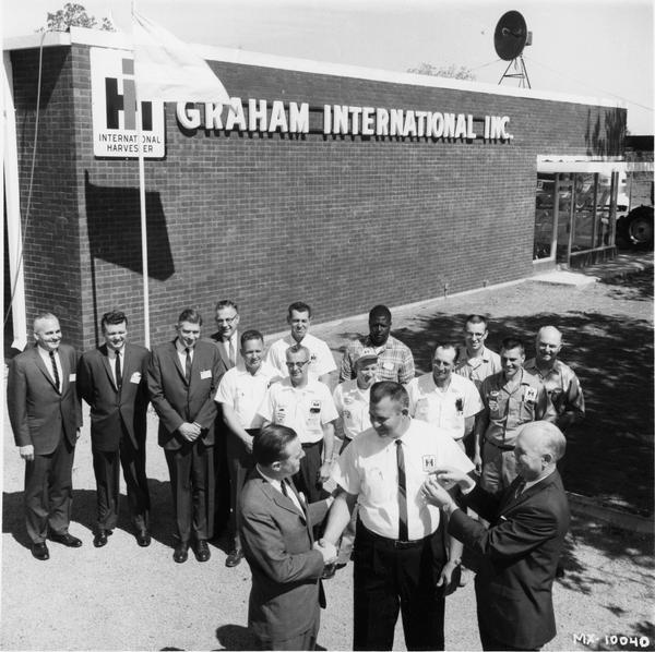 Original caption reads: "Congratulations are extended James Graham (center), the owner of Graham International, Inc., Sherman-Denison, Texas, one of the newest International truck dealerships in the country. E.A. Gibbs, (left) International Southwest regional sales manager, and C.T. Helin, Dallas district sales manager, do the honors as employees of the dealership and other IH executives look on. Graham International officially opened its doors May 1."