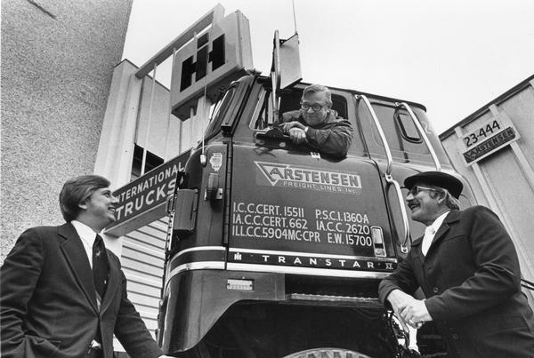 View of two International truck dealers posing with truck driver and International Transtar II in front of dealership. Truck was owned by Carstensen Freight Lines, Inc.