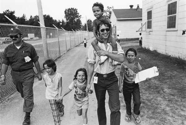 Interpreter Steve Gunderson, center, with four children and an unidentified man. Photographs made on July 4, 1980, by Archibald of Cuban refugees who had arrived as a result of the Port of Mariel exodus, and were housed at Camp McCoy, Wis.; including images of the camp life of Cuban men, women, and children.