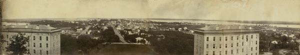 Panoramic view of Madison from Main Hall, now Bascom Hall, on the University of Wisconsin campus. North Hall and South Hall are in the foreground. Lake Mendota, the second Wisconsin State Capitol building, and Lake Monona are in the distance. Between campus and the lakes are numerous residences, including the Farwell House, several churches, and businesses around the capitol.