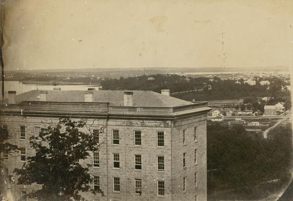 View of Madison from Main Hall, now Bascom Hall, on the University of Wisconsin-Madison campus. North Hall is in the foreground with several residences and Lake Mendota behind.  A small portion of Lake Monona, a church steeple, and the Farwell House are in the distance.