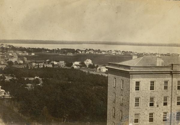 View of Madison from Main Hall, now Bascom Hall, on the University of Wisconsin-Madison campus.  South Hall is in the foreground with several residences and Lake Monona behind.