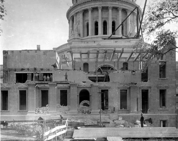 Workmen stand atop and in front of the remnants of the last remaining wing, the North Wing, of the third Wisconsin State Capitol building.