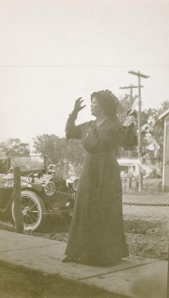 Belle Case La Follette, the wife of Robert M. La Follette, Sr., wearing a black dress and hat and speaking outdoors at an unidentified location.