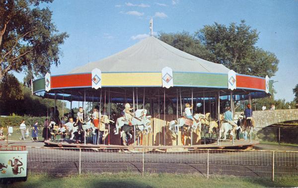 Children riding the carousel (merry-go-round) at Henry Vilas Zoo (Vilas Park Zoo), donated by the citizens of the Madison area. A stone bridge is in the background on the right.