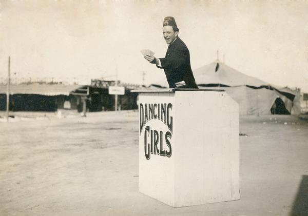 Dell Hammel offering tickets for a Shriner Circus sideshow of Dancing Girls. There are good indications that this photograph has been manipulated and is a composite of two images.