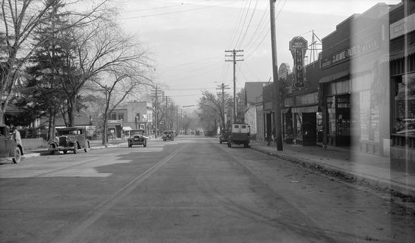 View up Monroe Street, looking northeast toward the University of Wisconsin-Madison campus, showing the intersection with Spooner. Also visible are cars, signs for Highway 18, and Beck-Purcell Shoes at 1849 Monroe Sreet, which was owned by Joseph P. & Mary B. Beck and John V. Purcell from 1935-1937.