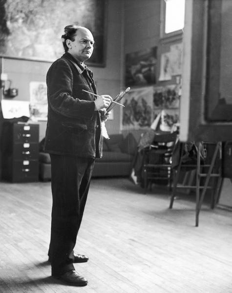 Candid portrait of John Steuart Curry working in his studio, holding paintbrushes.