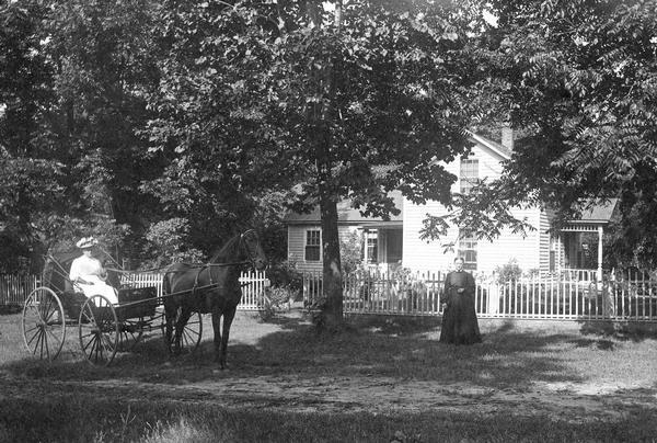 Mrs. Goodhue and Alletta pose in front of the Goodhue family residence, one of them in a horse-drawn carriage.