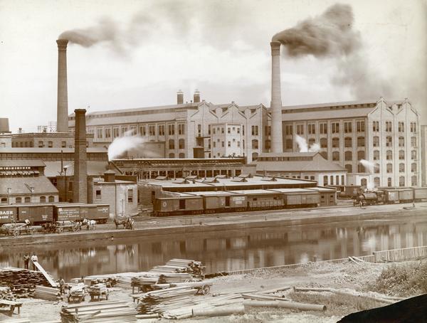 Southwest panorama of the McCormick Reaper Works factory and rail yard as seen across a canal. Workers can be seen unloading wood.