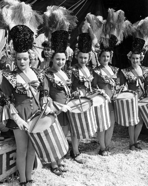 Five women drummers with the Ringling Brothers, Barnum and Bailey Circus posing with striped drums. They are wearing band uniforms, including large hats topped by plumes.