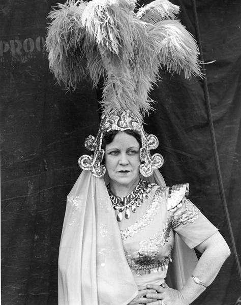 A female Cole Brothers Circus performer is shown in costume, wearing a tall plumed hat, with a tent as a backdrop.