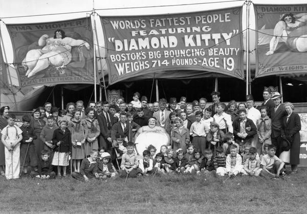 "Diamond Kitty," a performer with the Shrine Circus, poses with a large group of people in front of the sideshow tent housing the "World's Fattest People" attraction.
