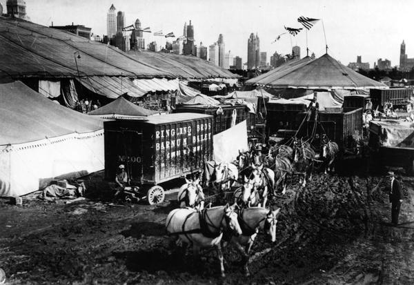 Elevated view of Ringling Brothers circus wagons, horses, and tents, with the Chicago skyline in the background.