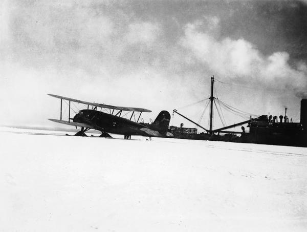 Curtiss-Wright Condor biplane named "William Horlick" outfitted with skis for use during Adm. Richard E. Byrd's second Antarctic expedition, 1933-35.  The supply ship "Jacob Ruppert" is in the background. This is a copy made by Edward T. Billings; the original photographer is unknown.