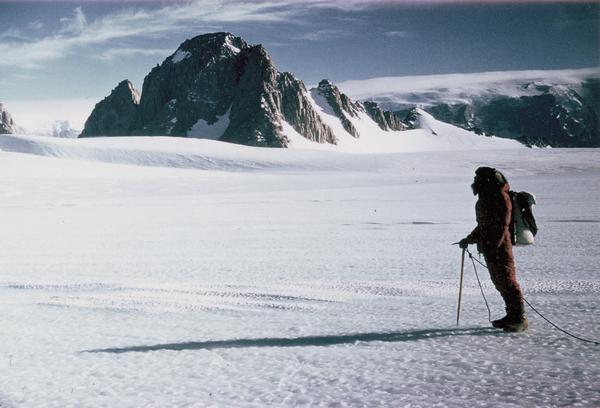 Unidentified explorer standing in field of snow with the Horlick Mountains of Antarctica in the background. The Horlick Mountains were named by Admiral Richard E. Byrd for William Horlick of Racine, Wisconsin, who helped finance his expeditions.
