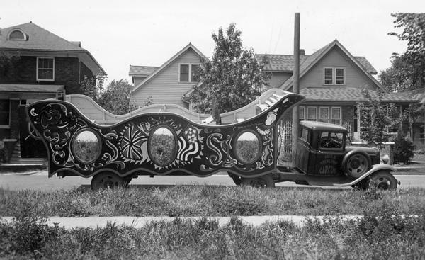A circus wagon, hitched to a truck cab, is parked across the street from three houses in a residential neighborhood.