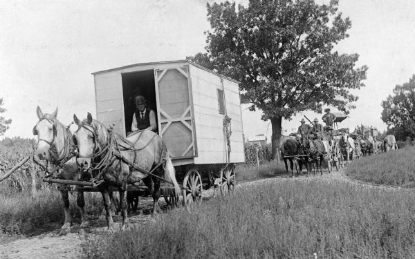 George W. Hall, Jr.'s wagon show, pulled by horses, travels along a country road.
