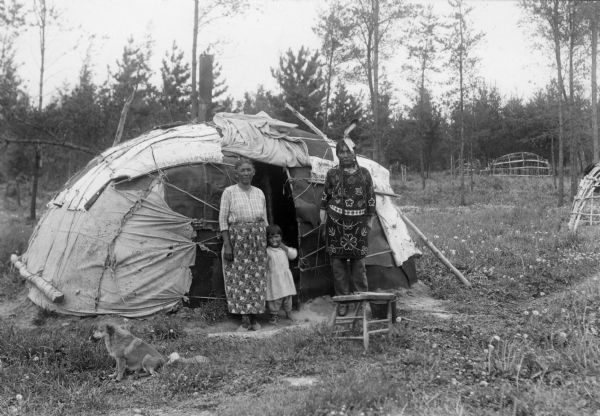 Chippewa (Ojibwa) medicine man John King, with his wife, grandchild, and family standing near a birch wigwam on the Lake Court Oreilles reservation. John King resided in a nearby log cabin and the traditional dwellings were used for traditional ceremonial gatherings. This image is part of an exhibit about Native Americans prepared by Paul Vanderbilt, the first curator of photography at the Wisconsin Historical Society.