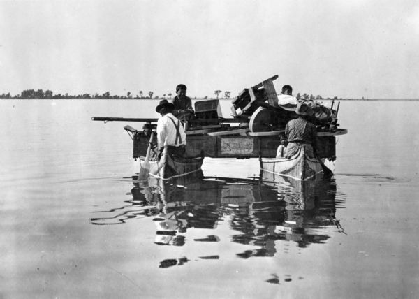 A Chippewa (Ojibwa) family moving their disassembled wagon and grindstone from one village to another on two canoes somewhere in northern Wisconsin. This image is part of an exhibit about Native Americans prepared by Paul Vanderbilt, the first curator of photography at the Wisconsin Historical Society.