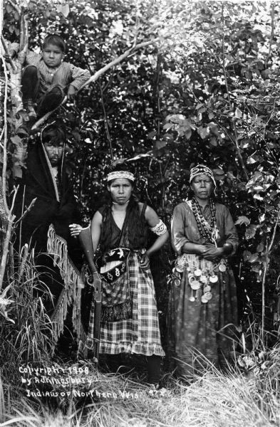 A Chippewa (Ojibwa) group wearing traditional clothing photographed by A.J. Kingsbury, a photographer who produced many "documentary" postcards. This image is part of an exhibit about Native Americans prepared by Paul Vanderbilt, the first curator of photography at the Wisconsin Historical Society. Caption at bottom left reads: "Indians of Northern Wis."