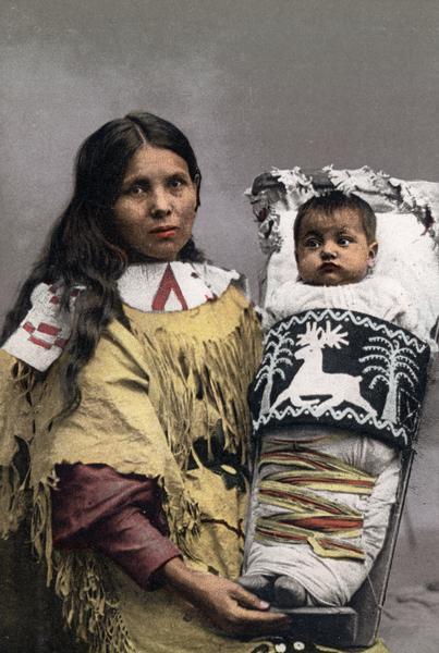 Hand-colored photograph depicting a Native American mother holding her child in a cradleboard.  This image is part of an exhibit about Native Americans prepared by Paul Vanderbilt, the first curator of photography at the Wisconsin Historical Society.