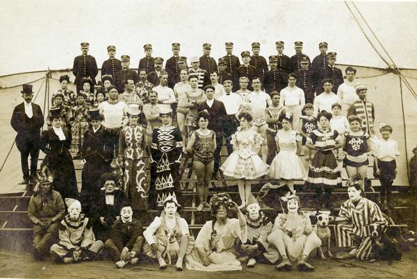 A group portrait of Norris & Rowe circus performers outside a tent at winter quarters, including clowns, riders, and high wire performers.