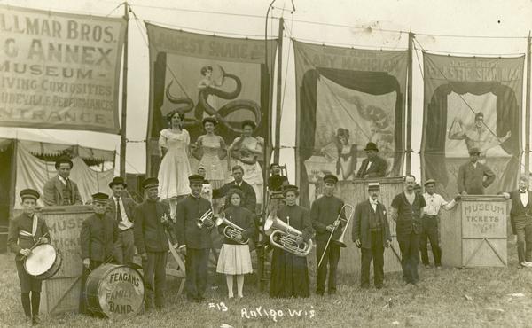 Musicians with the Gollmar Brothers Circus pose in front of banners advertising the circus sideshow features near the entrance to the museum annex tent.