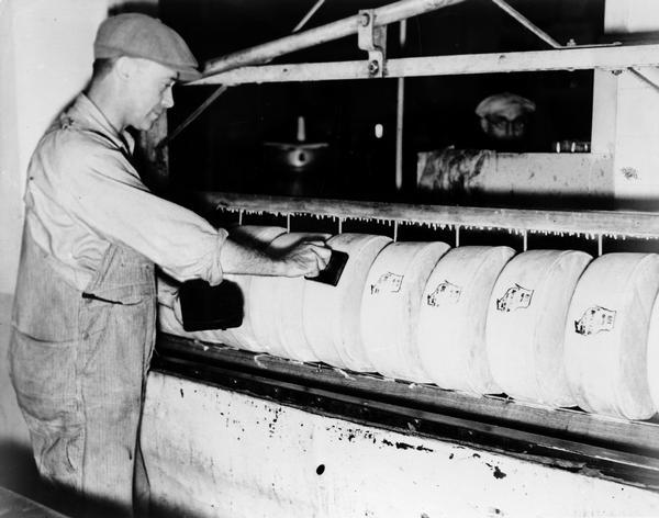 A male worker in a cheese-making factory places a Wisconsin stamp on cheeses.