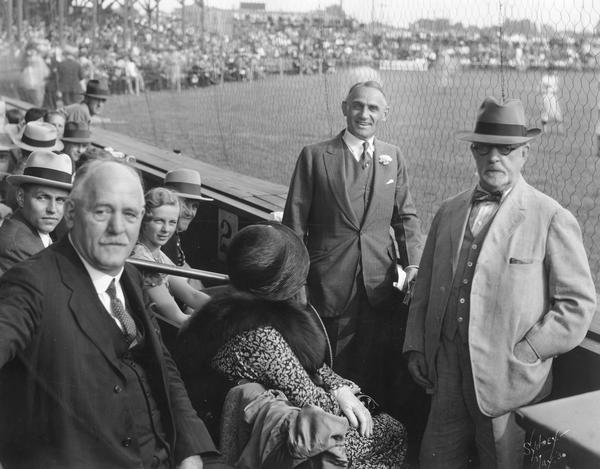 Governor Walter J. Kohler, Sr., (with flower in his lapel), who was campaigning for re-election, took time out for a baseball game at Horlick Athletic Field in Racine, Wisconsin. With him, on the far left is his son, John M. Kohler, State Senator Walter S. Goodland of Racine, who would later become governor of Wisconsin, and William Horlick, Jr.  Other individuals in the photograph are unidentified. This game featured the then-World Champion Philadelphia Athletics vs. the Racine All-Stars.