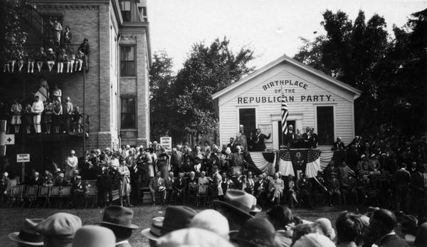 75th anniversary celebration of the birth of the Republican Party at Ripon. Governor Walter J. Kohler, Sr., stands on the podium in front of the Little White Schoolhouse to the right of the microphone.