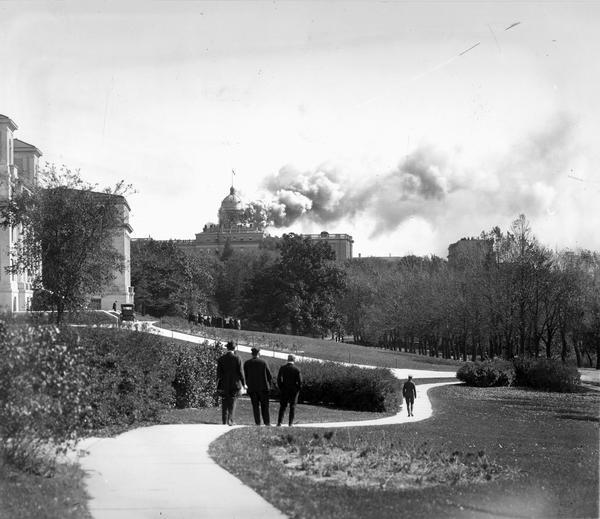 People walking along the Linden Drive path watch as Bascom Hall (formerly Main Hall) dome burns on the University of Wisconsin-Madison campus. Fire destroyed the ornate dome.