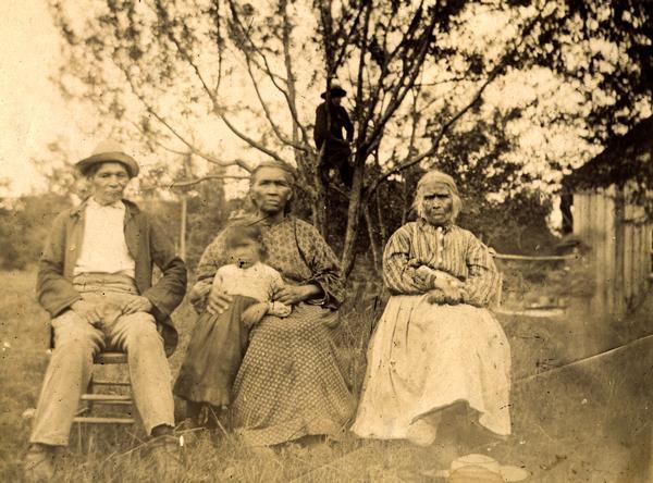 A Potowatomi group consisting of David Nsa-waw-quet, his wife Margaret Nsa-waw-quet, and her sister Mary Wabanosay, or "Morning Walking." A young girl is standing next to the woman in the center. Another person is perched in a tree in the background. This image is part of an exhibit about Native Americans prepared by Paul Vanderbilt, the Wisconsin Historical Society's first curator of photography.