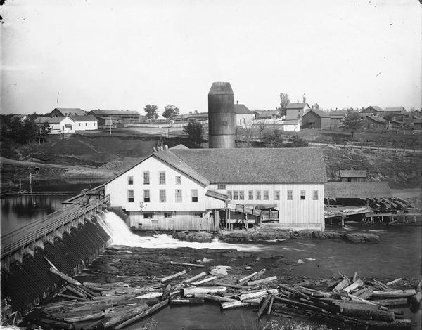 Knapp-Stout and Company Sawmill on the Red Cedar River, with dam and logs in the foreground.