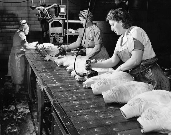 Women are stamping hams with the USDA grade stamp and the Oscar Mayer label as the hams move by on an assembly line.